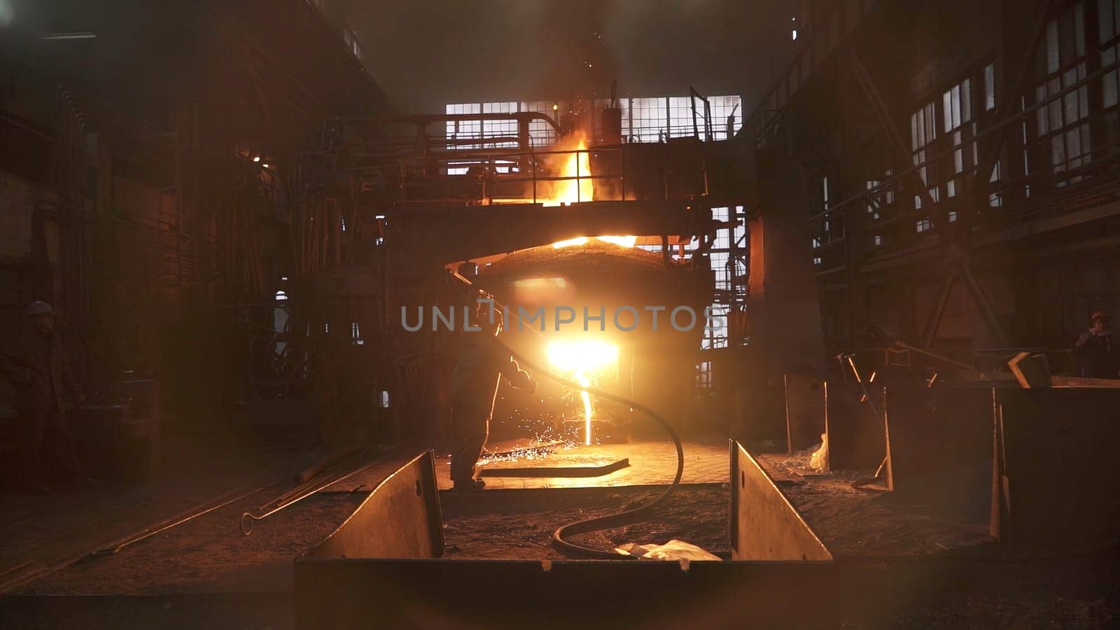 An industrial worker processing metal in a dimly lit foundry, creating a dramatic and intense scene. Stock Clip