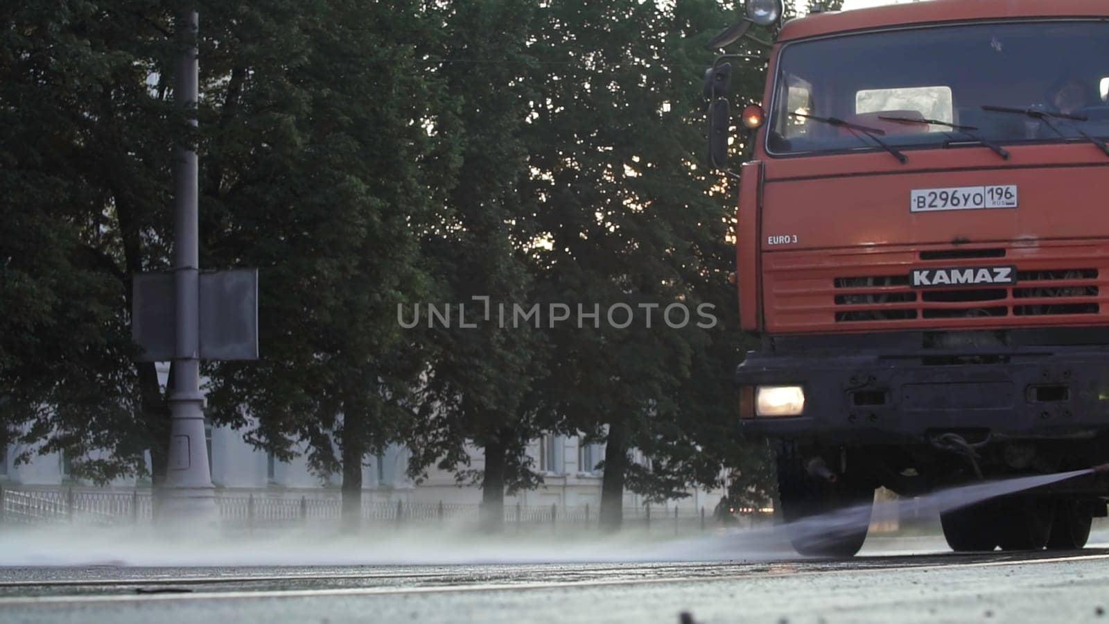 Tbilisi, Georgia - September 29, 2023: A bright red truck drives swiftly along a wet street, splashing up water as the sun rises behind the trees. Stock Clip