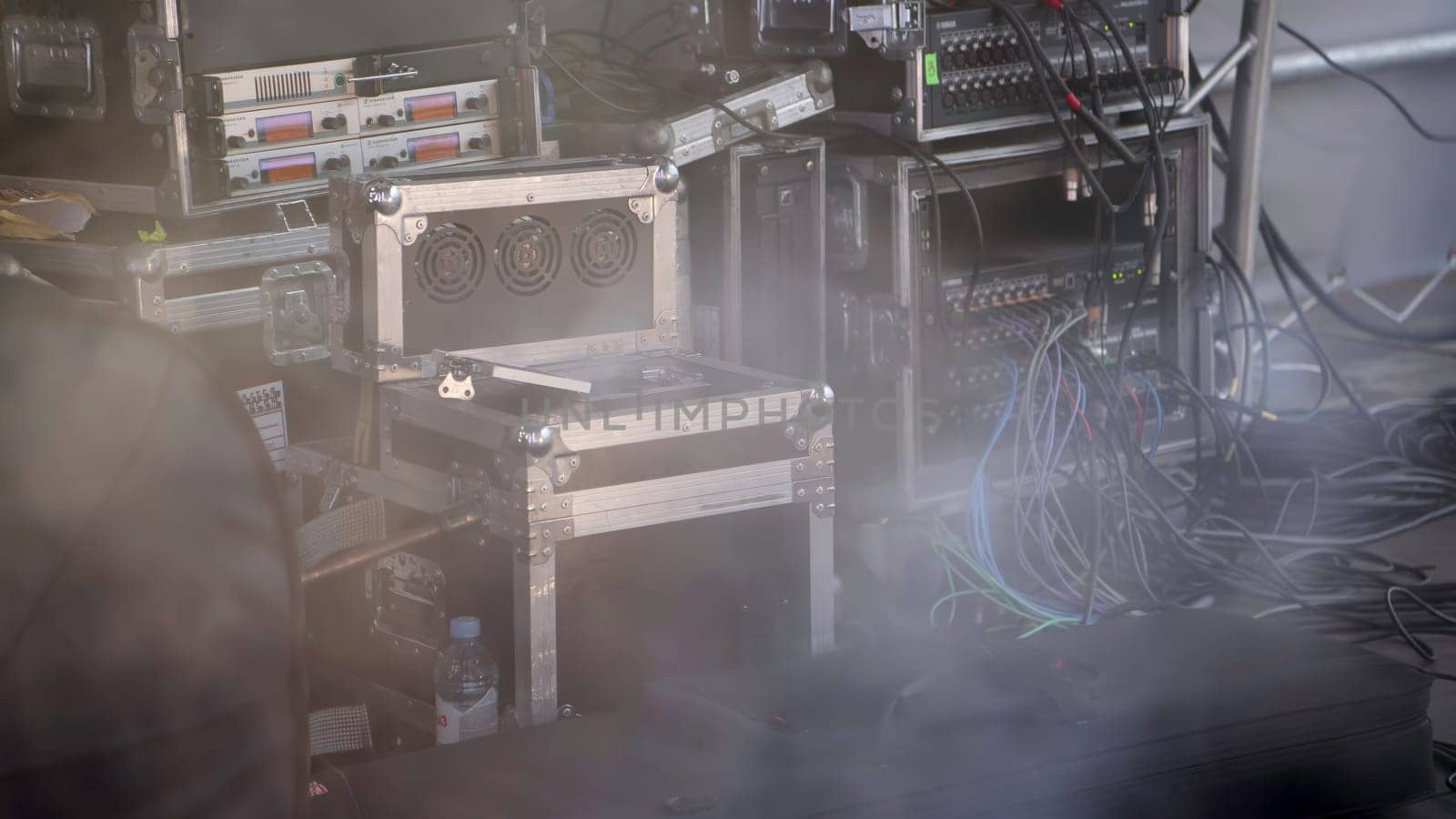A detailed closeup view of professional audio and lighting equipment set up backstage featuring cables and fog. Clip
