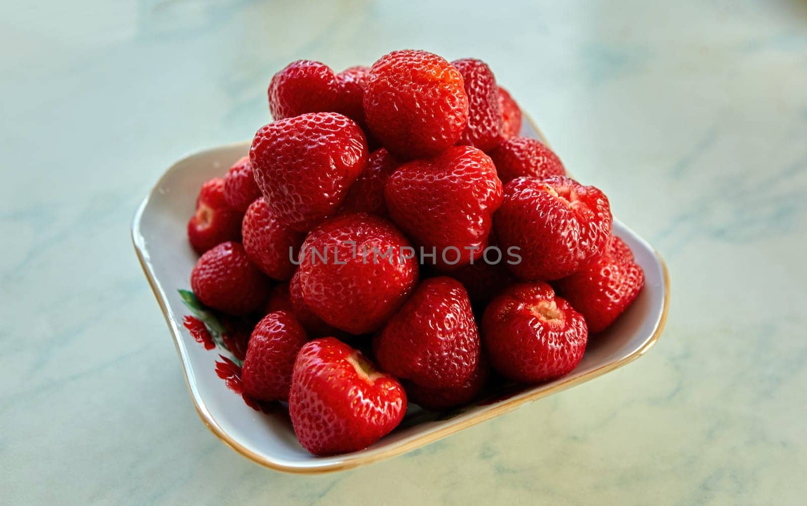A bountiful display of freshly picked strawberries arranged in a decorative porcelain bowl on a sunny kitchen countertop