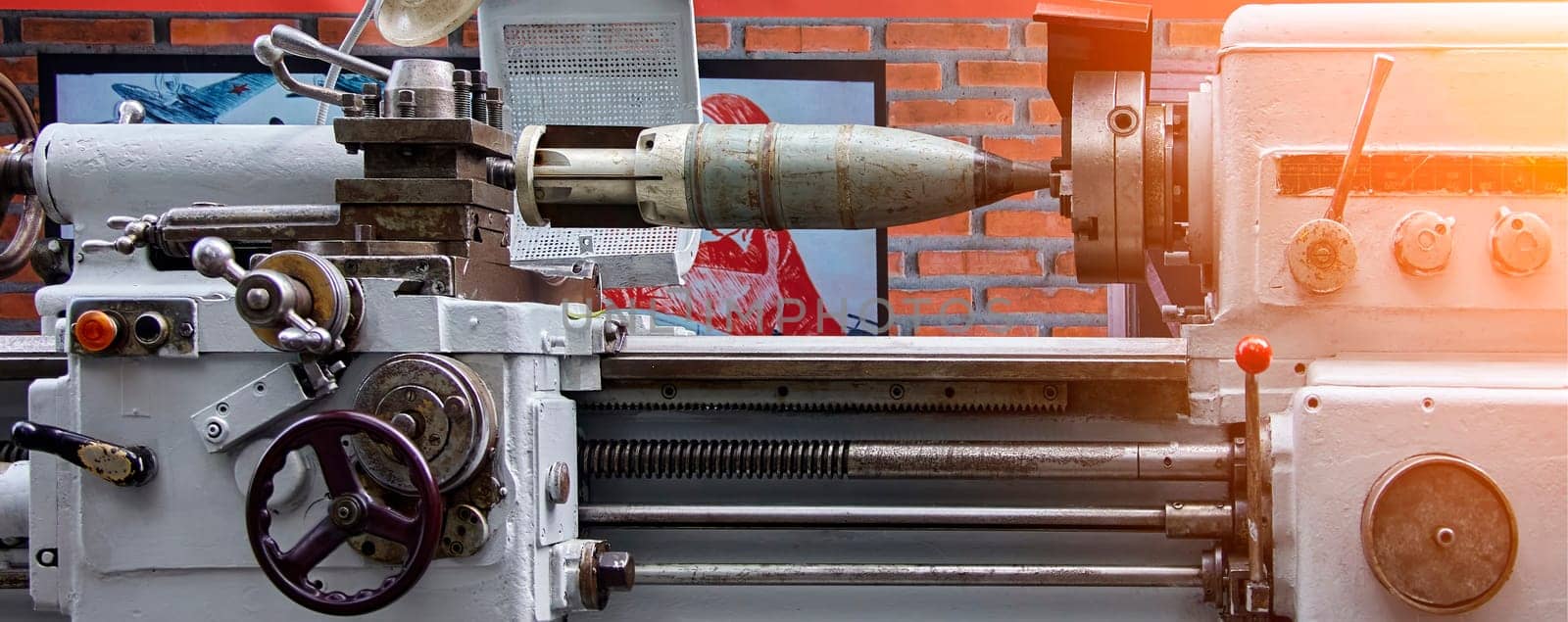 A powerful metalworking lathe is used to shape a large missile, its smooth surface gleaming under the workshop lights. The machine's intricate gears and levers are in motion, carefully guiding the tool as it spins against the metal. The workshop's brick walls add a touch of industrial character to the scene, emphasizing the raw power of the machinery.