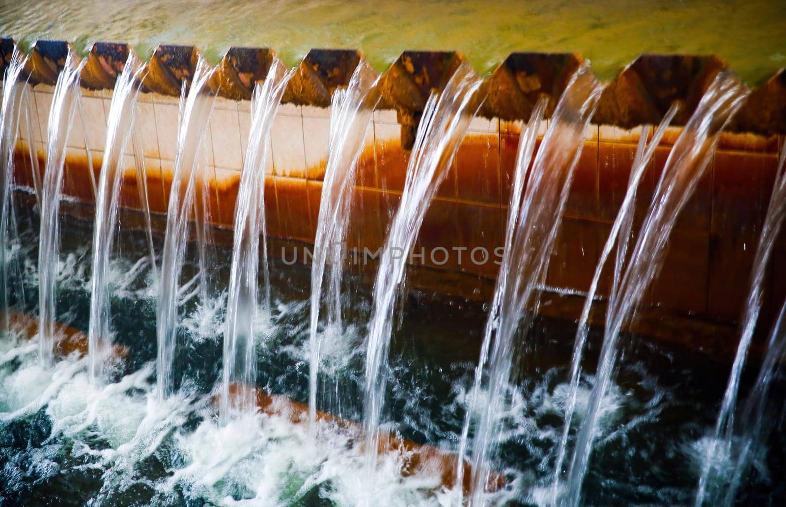 Water flows steadily over a stone ledge, creating a serene sound in a peaceful garden setting during the early morning.