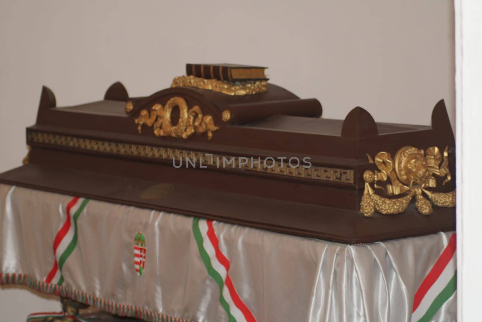 A beautifully carved wooden object rests on a table adorned with a decorative cloth featuring the Hungarian flag. The craftsmanship is evident in its intricate details and design.