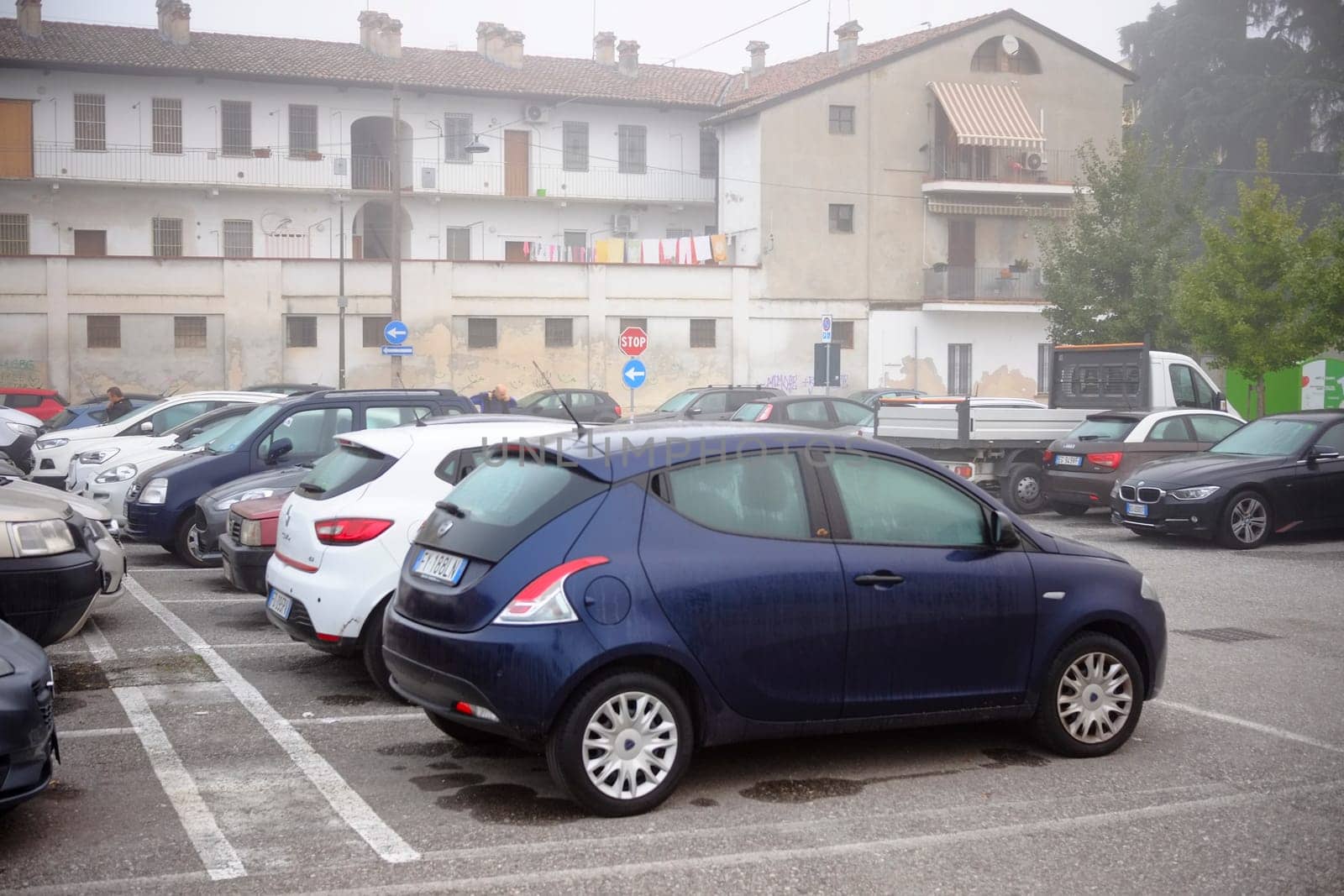 Cremona, Lombardy, Italy - November 7th 2024 Cars parked in parking lot in front of residential building on a foggy day