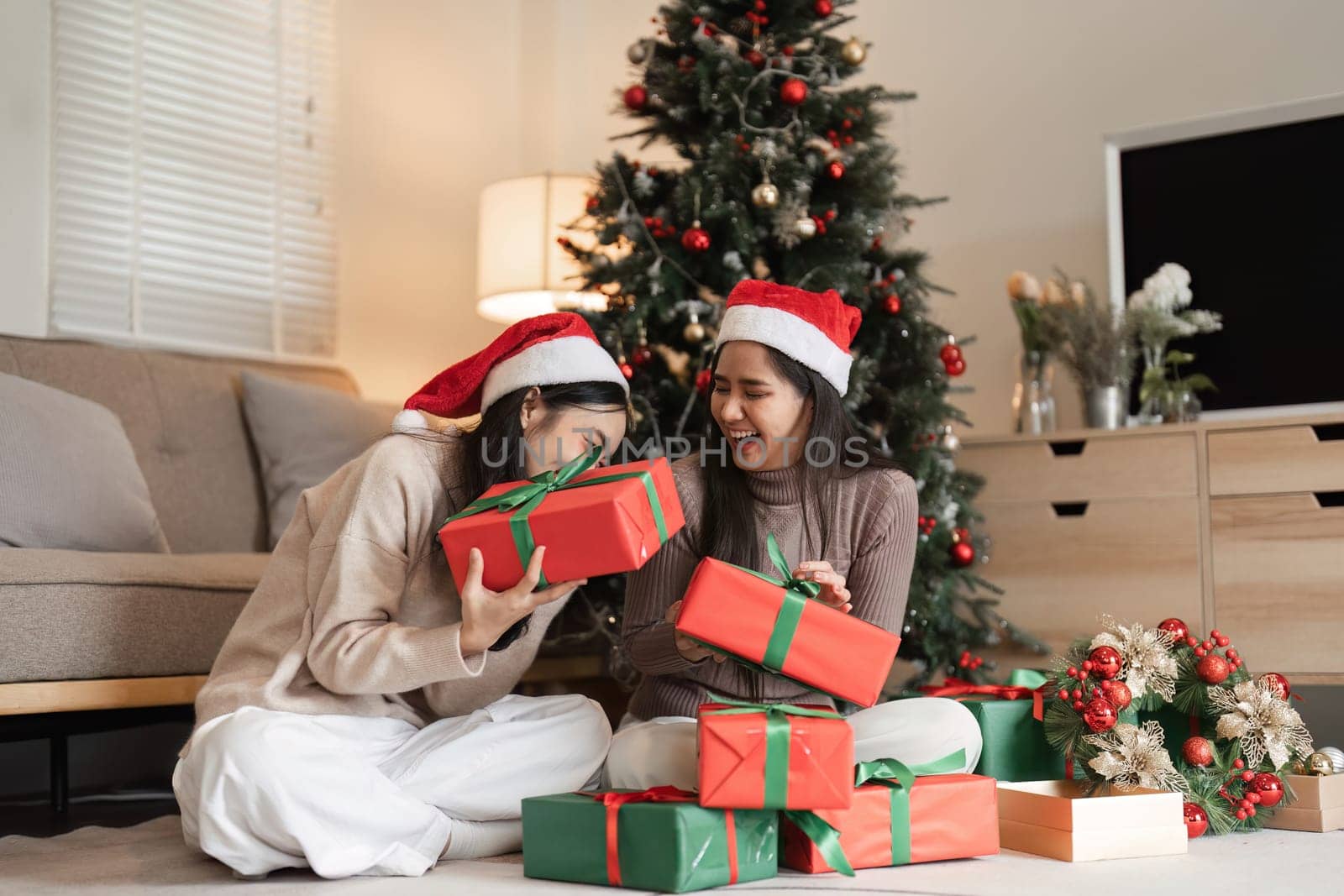 Two young women delight in exchanging surprise gifts on Christmas, surrounded by festive decorations and a beautifully adorned tree.