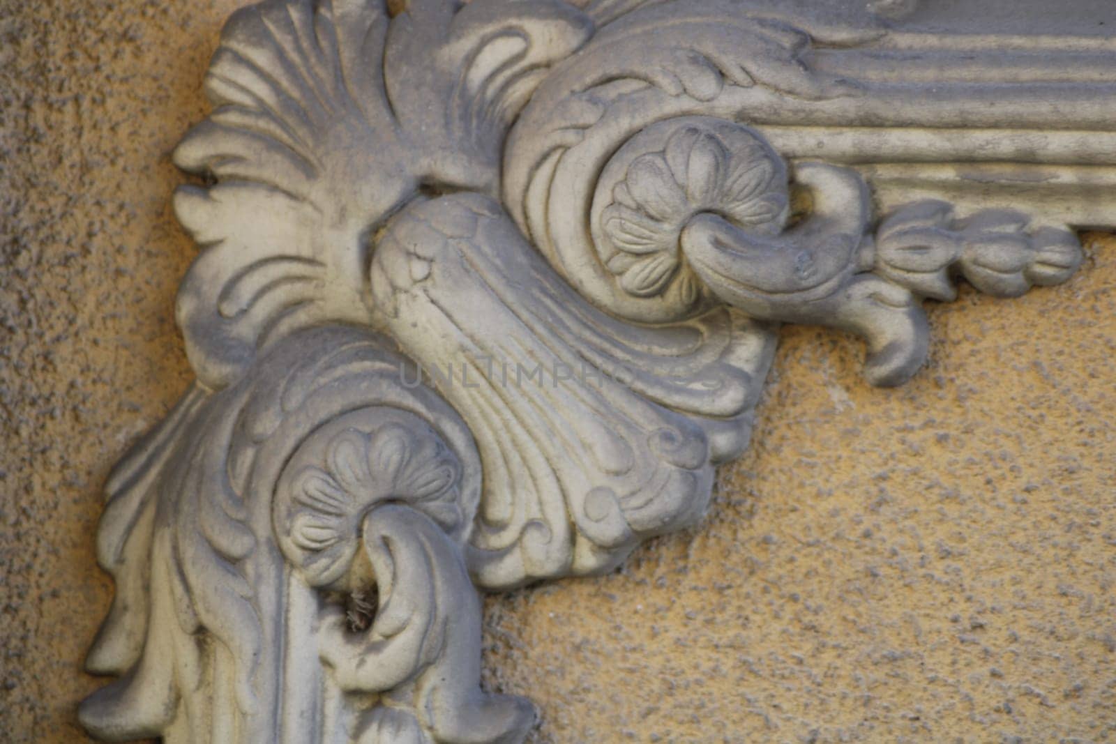 Intricate plaster work features elaborate floral motifs and curving lines, reflecting classic craftsmanship on an aged wall surface.