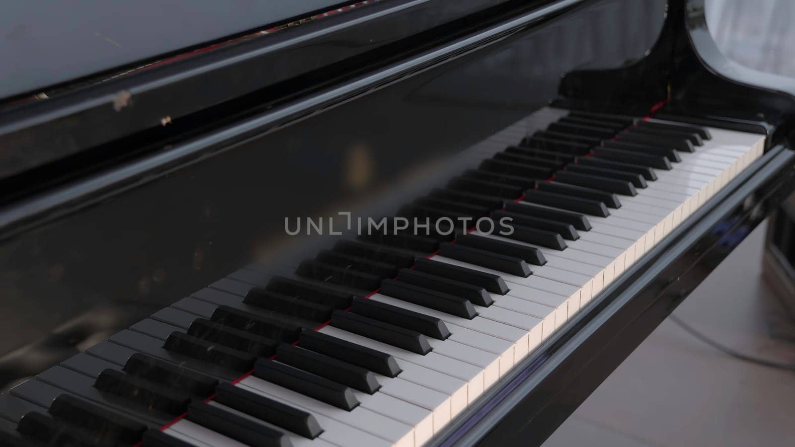 A closeup view of a grand piano beautifully showcasing its sleek black keys and its elegantly polished surface. Clip