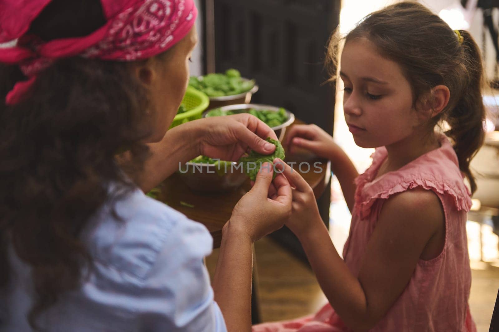 A mother and her young daughter share a moment while preparing fresh vegetables together. The scene exudes warmth, love, and family bonding, highlighting a tender teaching moment.
