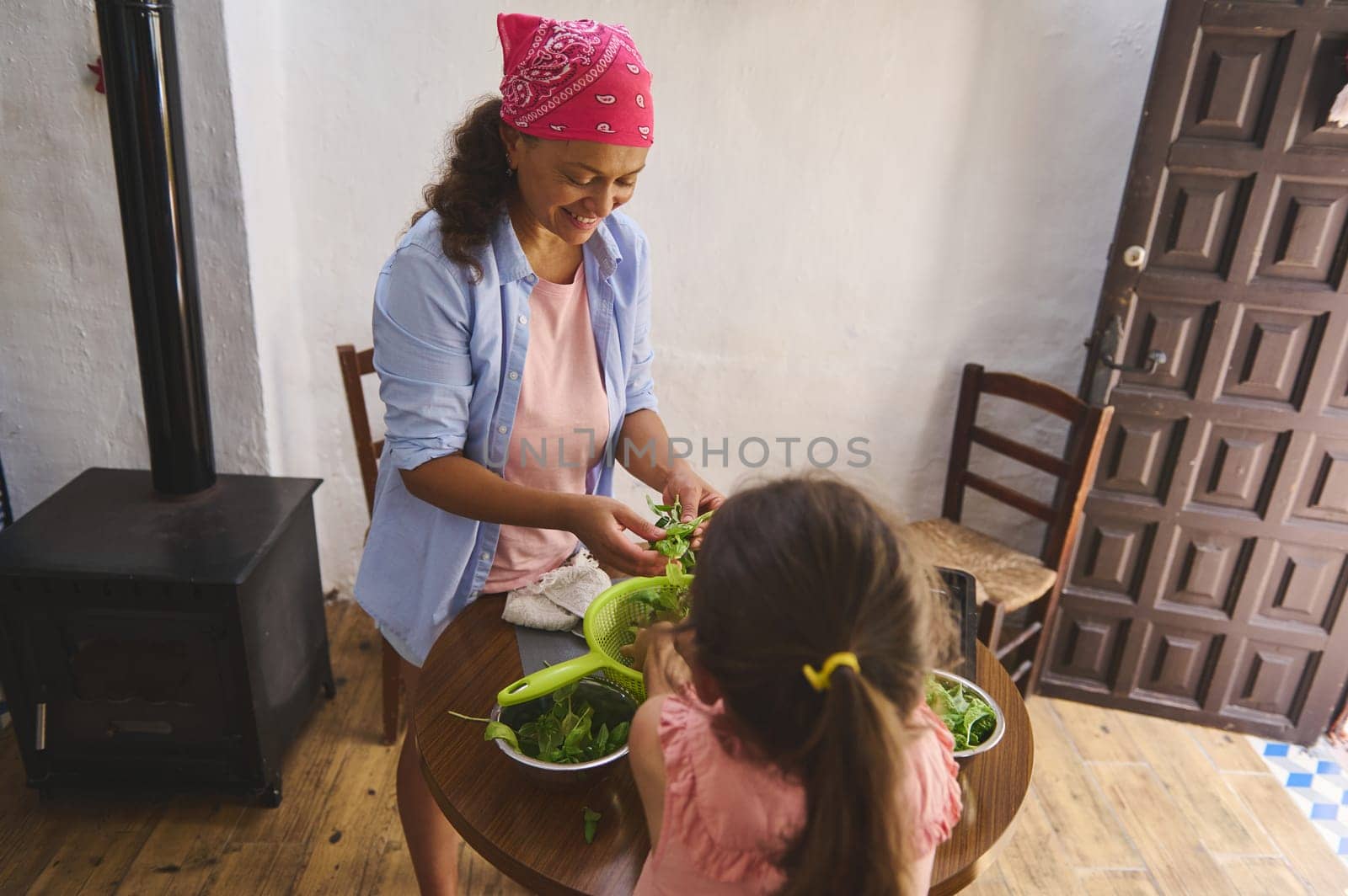 A cheerful mother and young daughter prepare a fresh green salad together in a cozy rustic kitchen, enjoying quality family time.