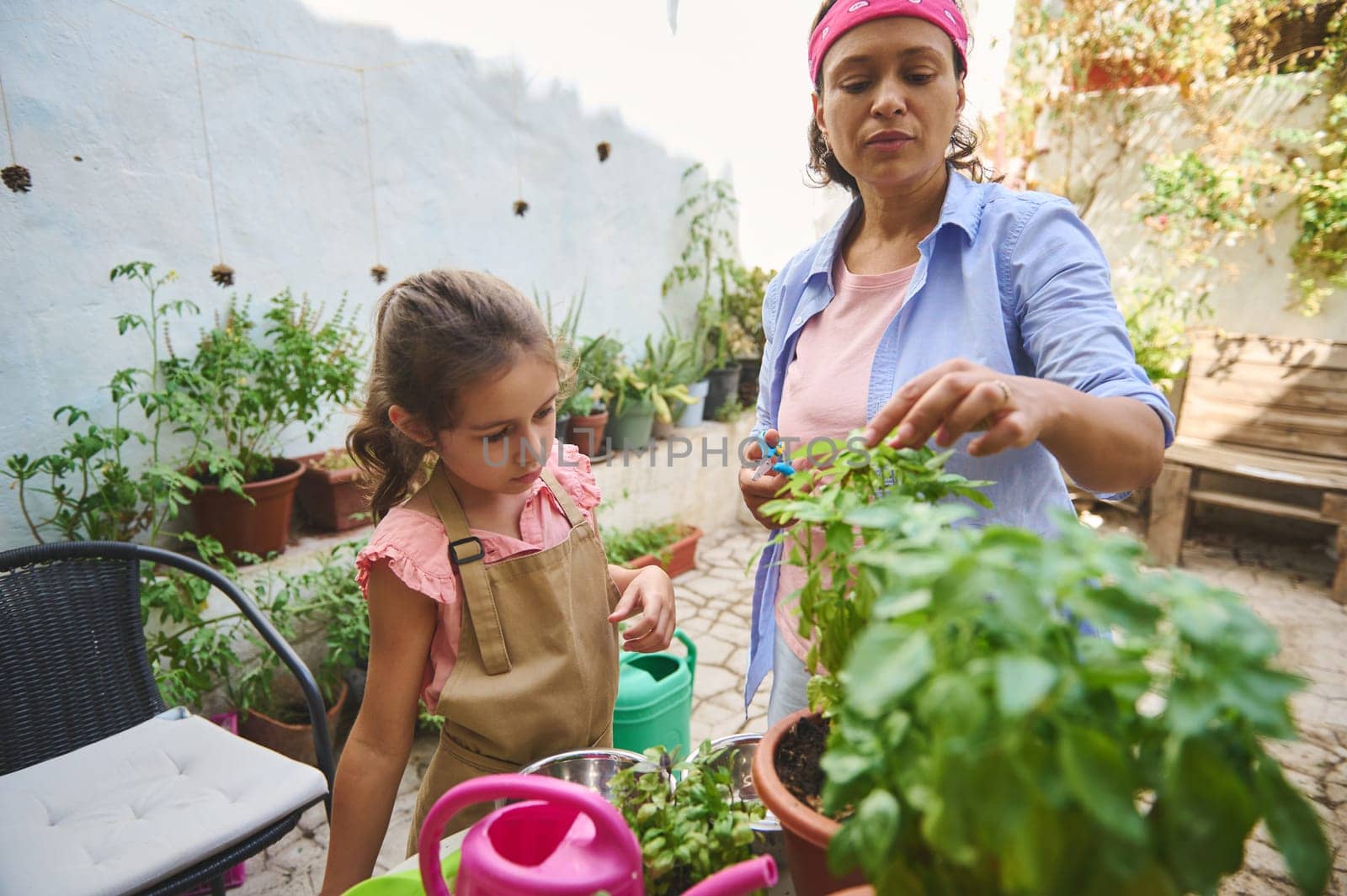 Mother and daughter enjoy a sunny day while tending to their garden. They share a moment of learning and nature as they care for plants in the backyard. Perfect for springtime themes.