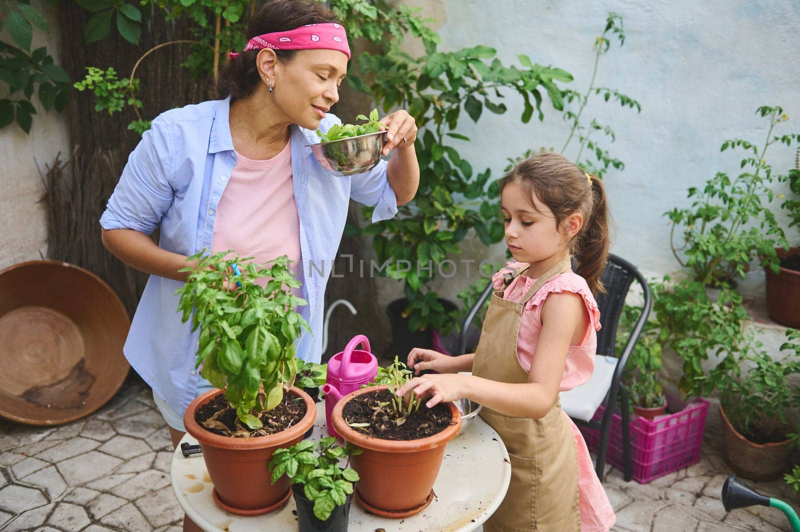 A mother and daughter enjoy gardening together, nurturing potted plants on a patio. They share a moment of learning and bonding, surrounded by nature.