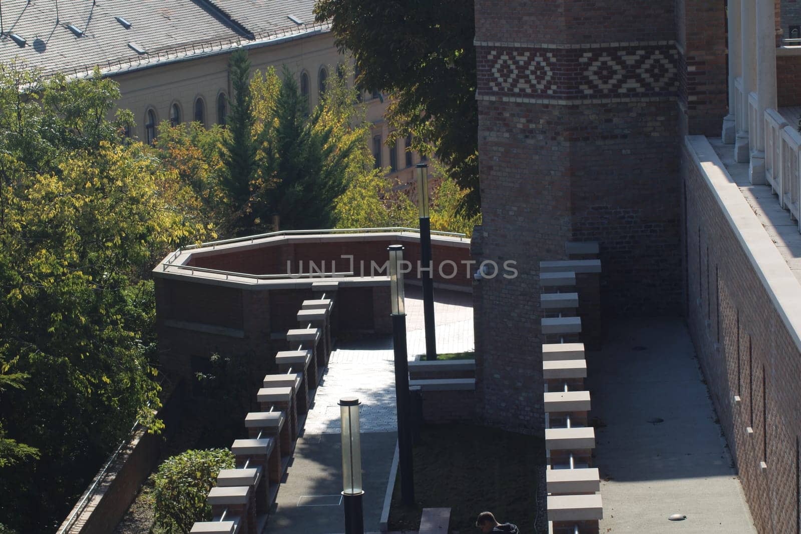 Visitors enjoy a peaceful outdoor space featuring benches and lush greenery next to a brick building under clear skies, capturing the essence of autumn.