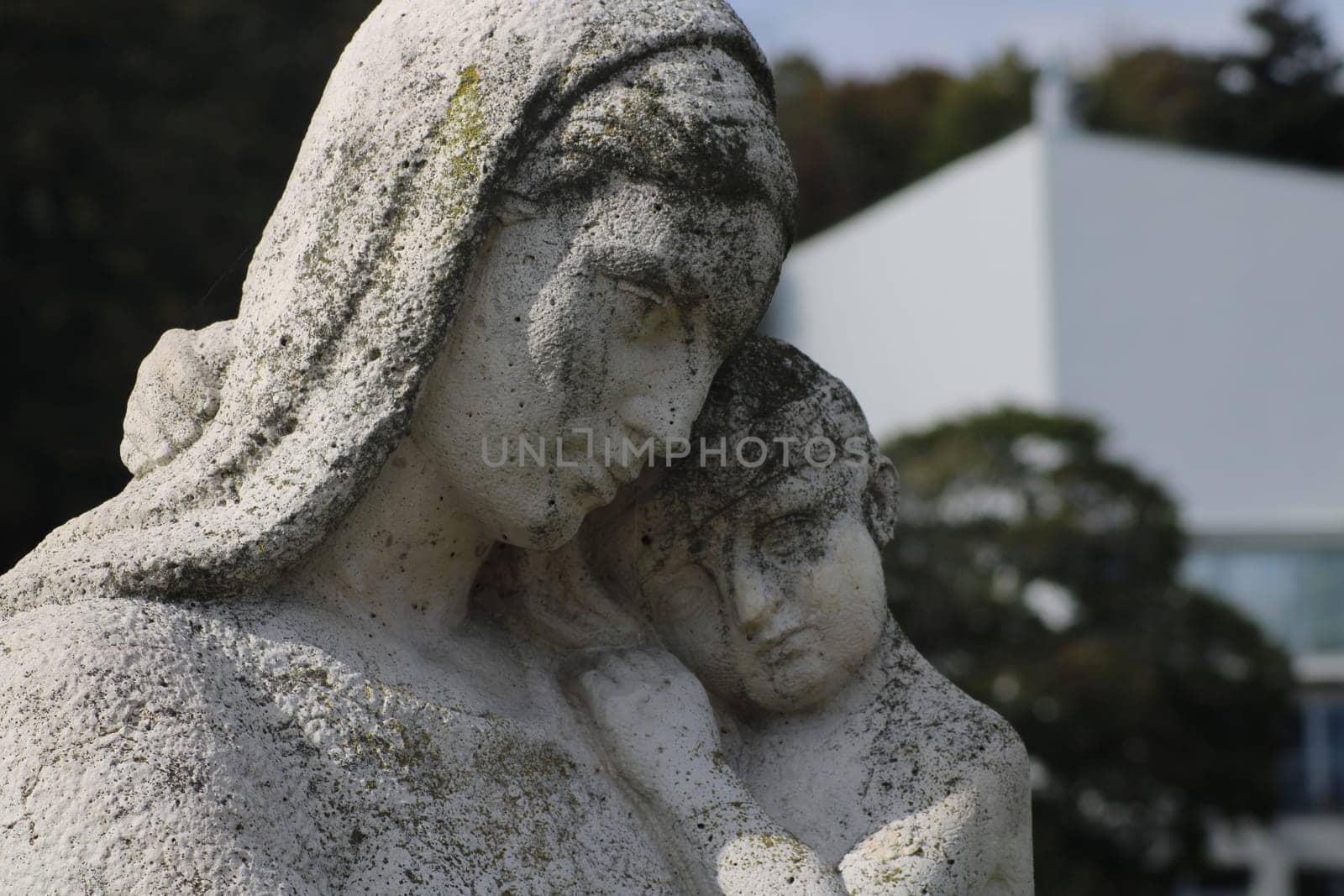 This artwork showcases a detailed sculpture of a mother and child, capturing a tender moment. The serene garden backdrop contrasts with the modern building behind, creating a unique atmosphere.