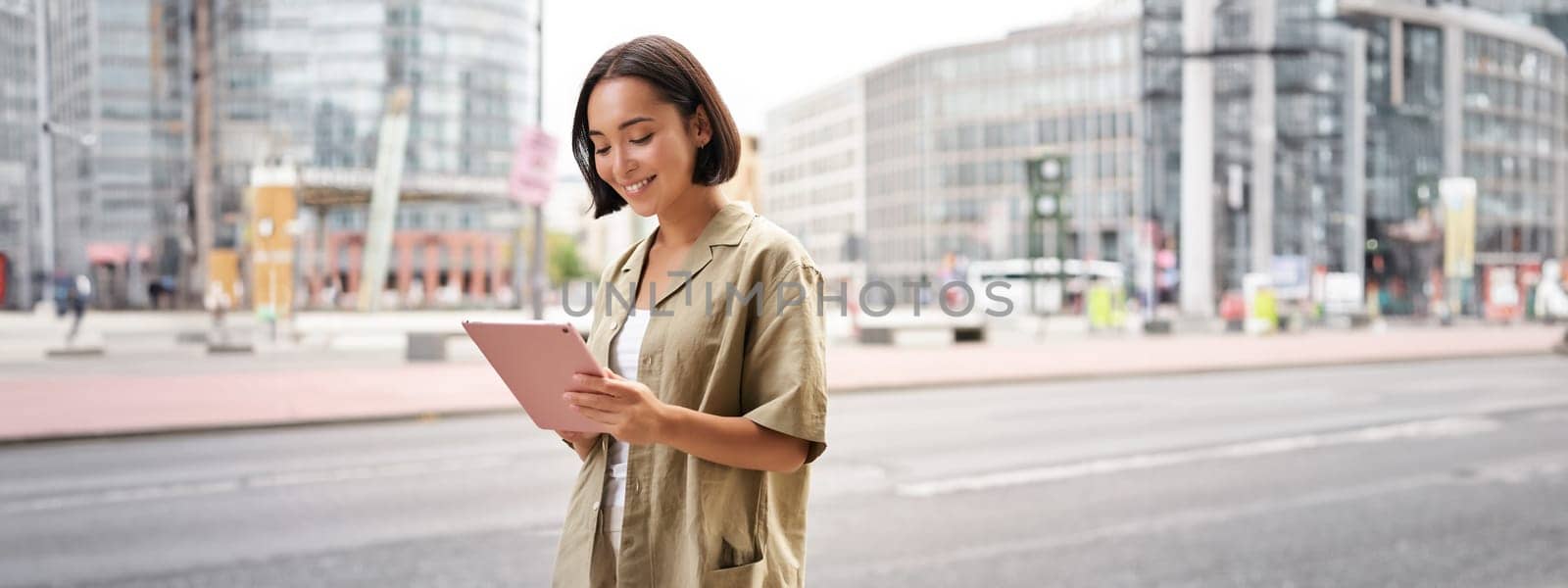 Portrait of young stylish woman walking with tablet, going somewhere in city.