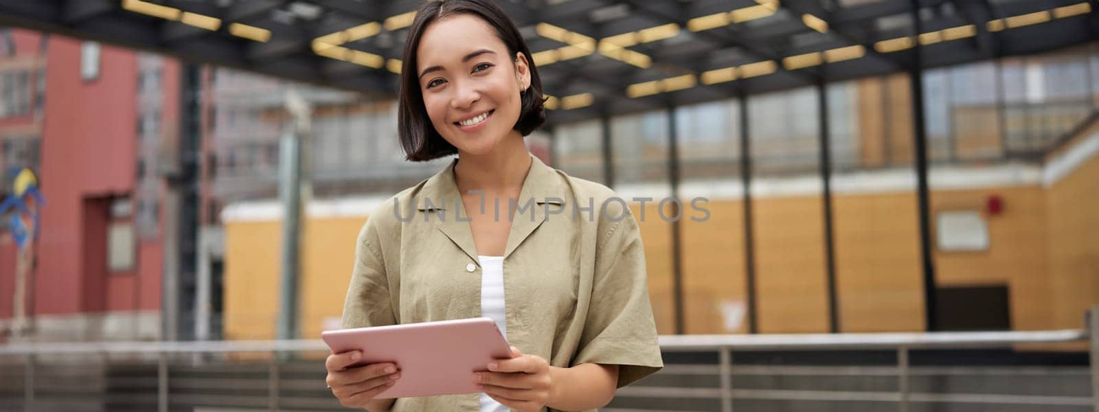 City girl standing with tablet on street, using application, smiling at camera by Benzoix