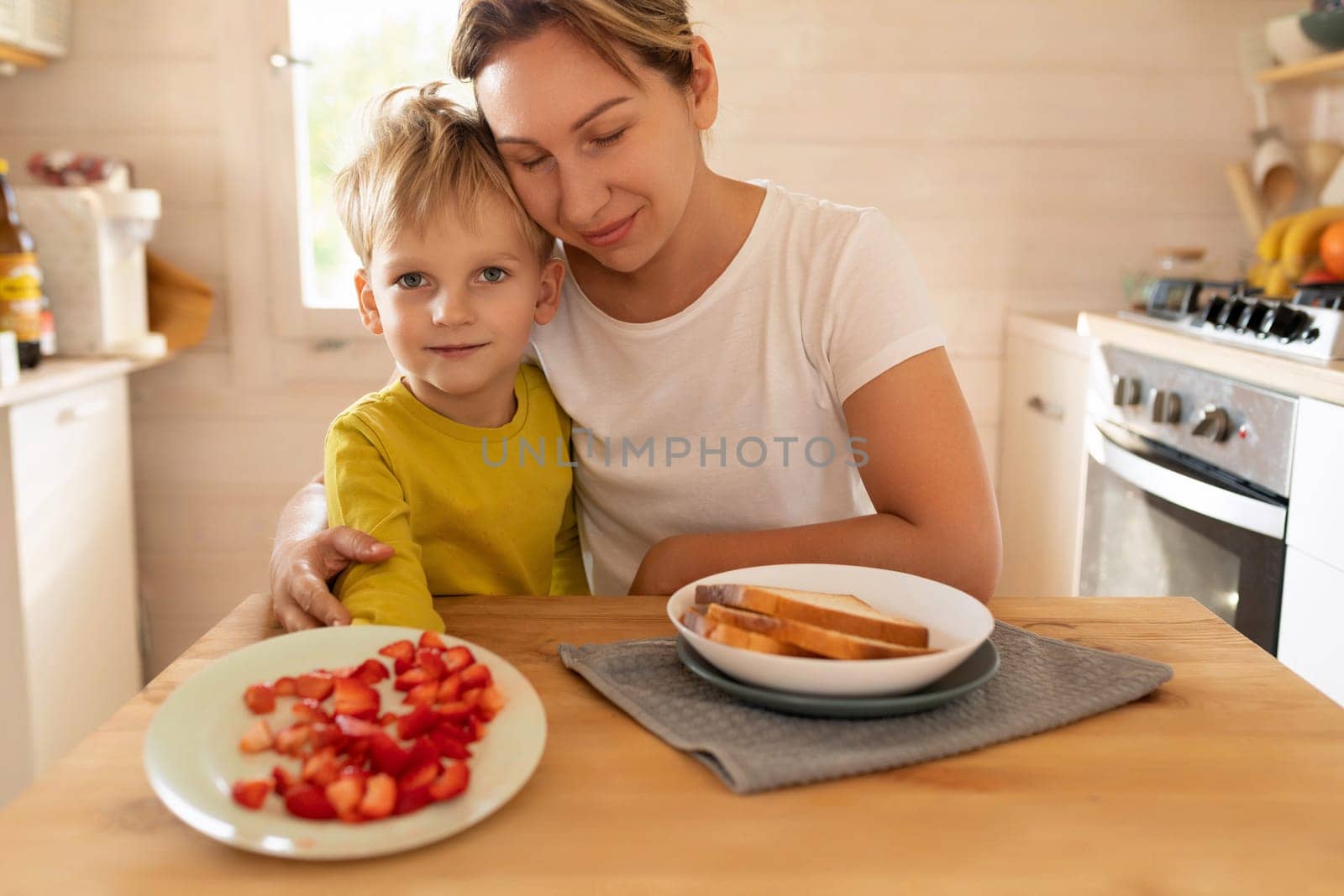 young mother and son sitting at the table and preparing breakfast at home, happy motherhood by TRMK