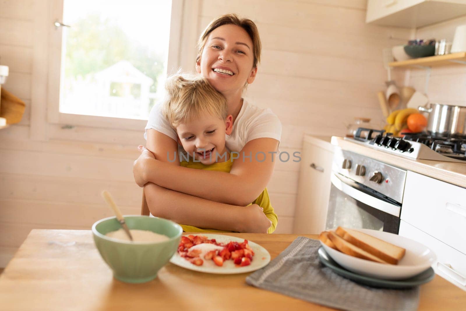cheerful Caucasian blond mother and child son are sitting in the kitchen and eating. happy childhood and motherhood.