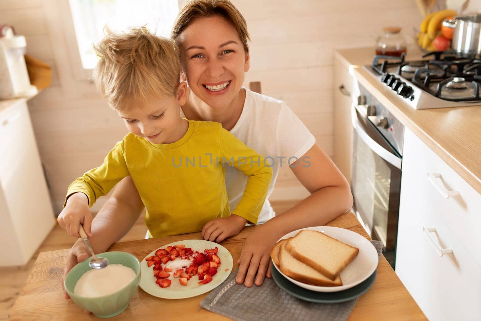 cheerful Caucasian blond mother and child son are sitting in the kitchen and eating. happy childhood and motherhood by TRMK