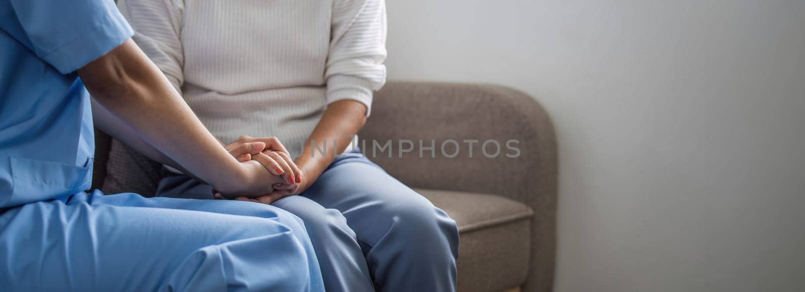 Happy patient is holding caregiver for a hand while spending time together. Elderly woman in nursing home and nurse.