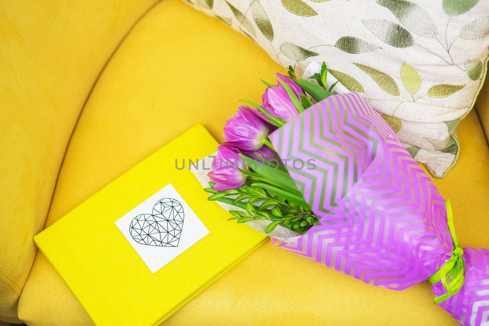 beautiful violet bouquet of tulips on a yellow stool and yellow book.