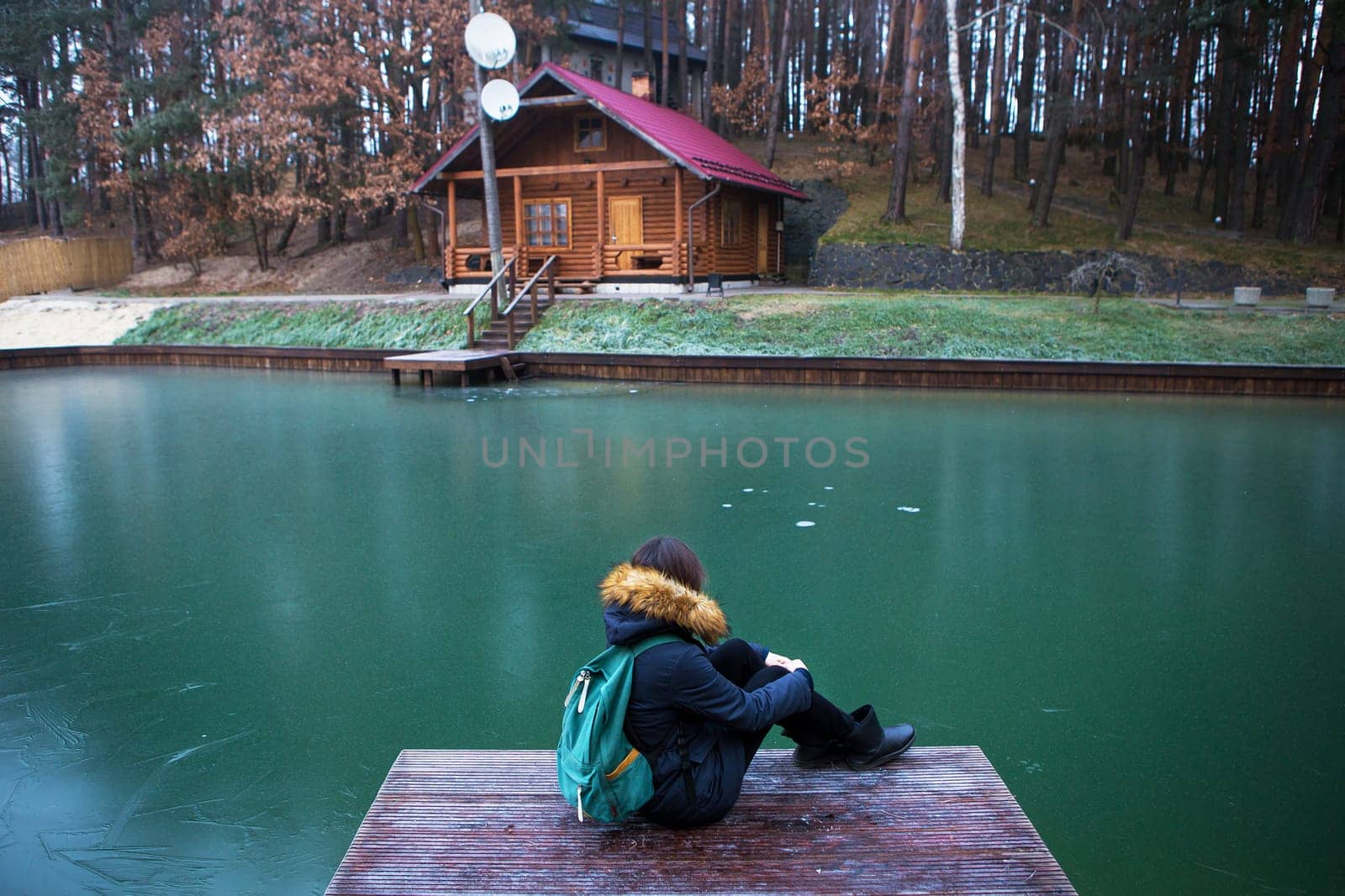 the girl is sitting with her back on a wooden bridge in a pine forest.