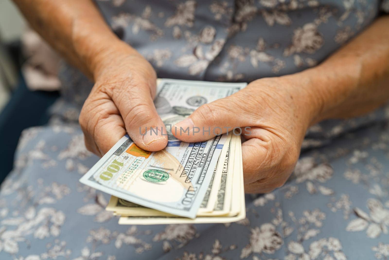 Asian senior woman holding and counting US dollar banknotes money in purse. Poverty, saving problem in retirement. by pamai