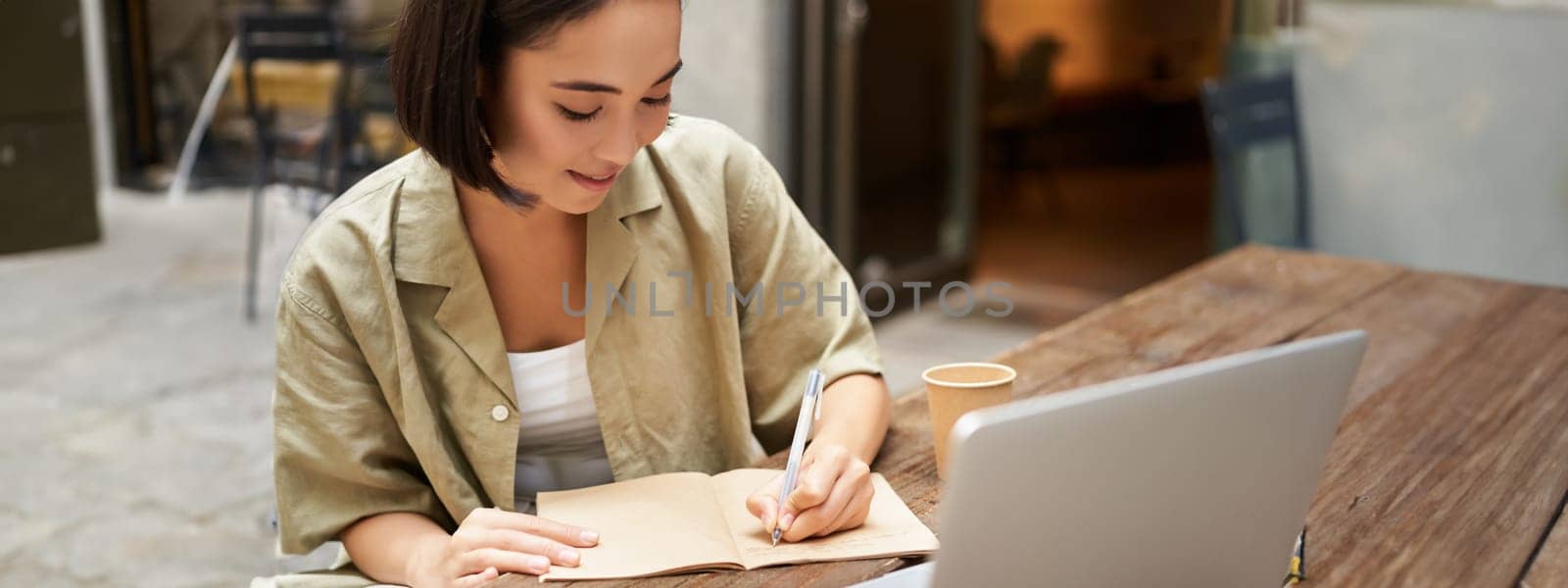 Portrait of young asian woman working on laptop, making notes, writing down while attending online lesson, work meeting by Benzoix