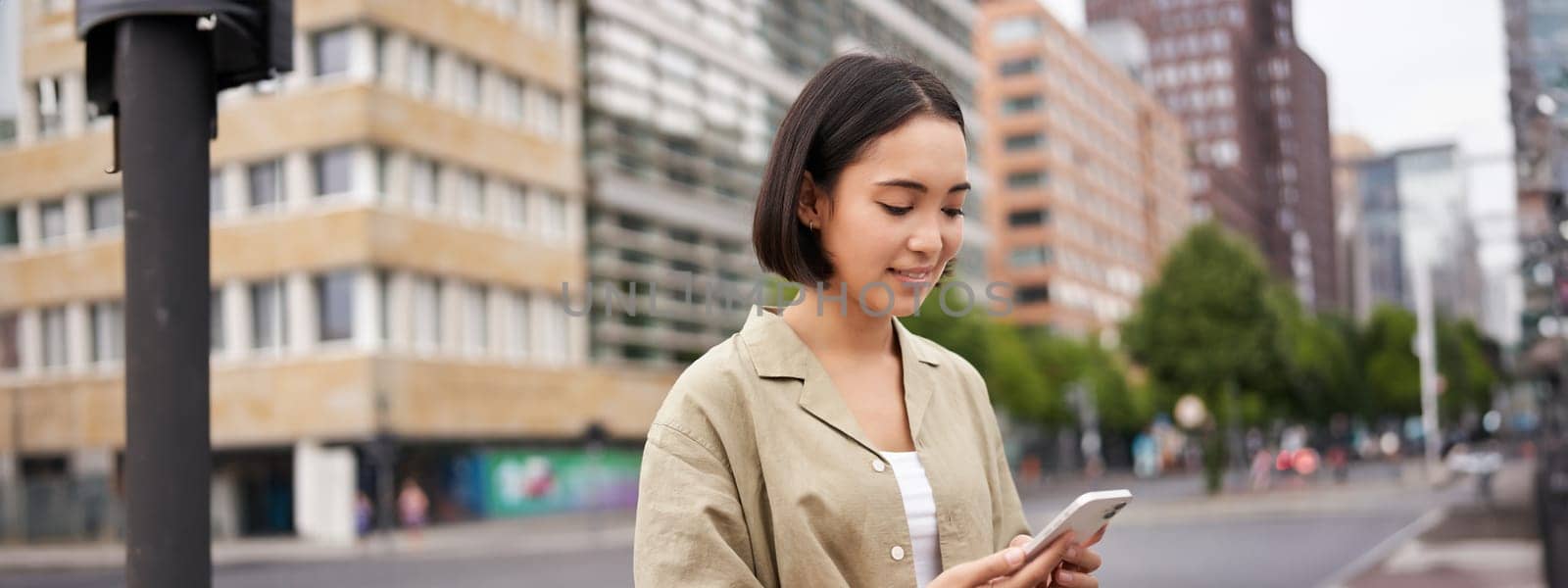 Young asian woman exploring city with smartphone app, holding mobile phone and walking on screet by Benzoix