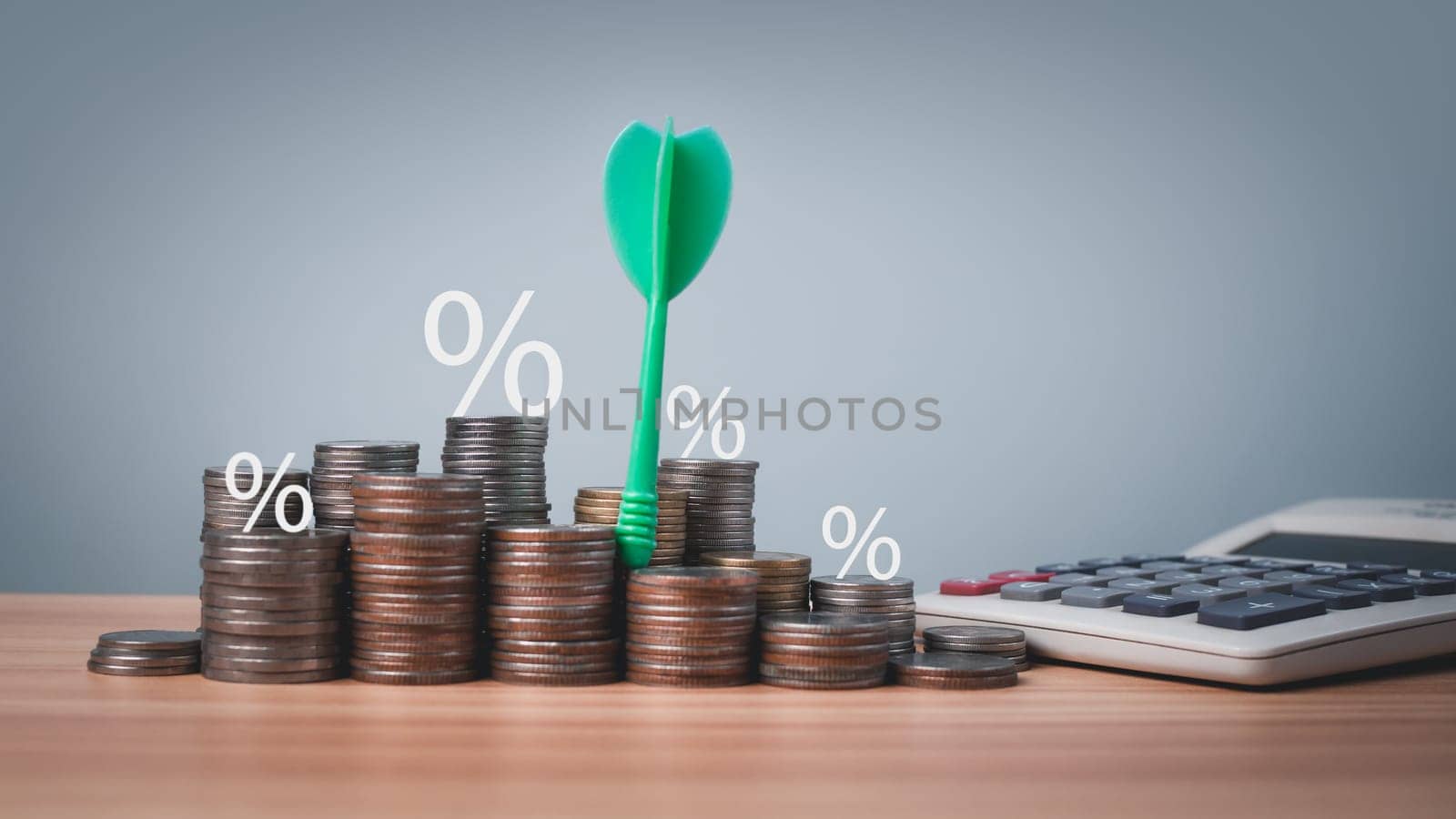 The green arrow hits the target in the center of a row of coins and calculator on the wooden floor. Concepts of finance, savings and investment. Business growth concept, finance goals concept. by Unimages2527