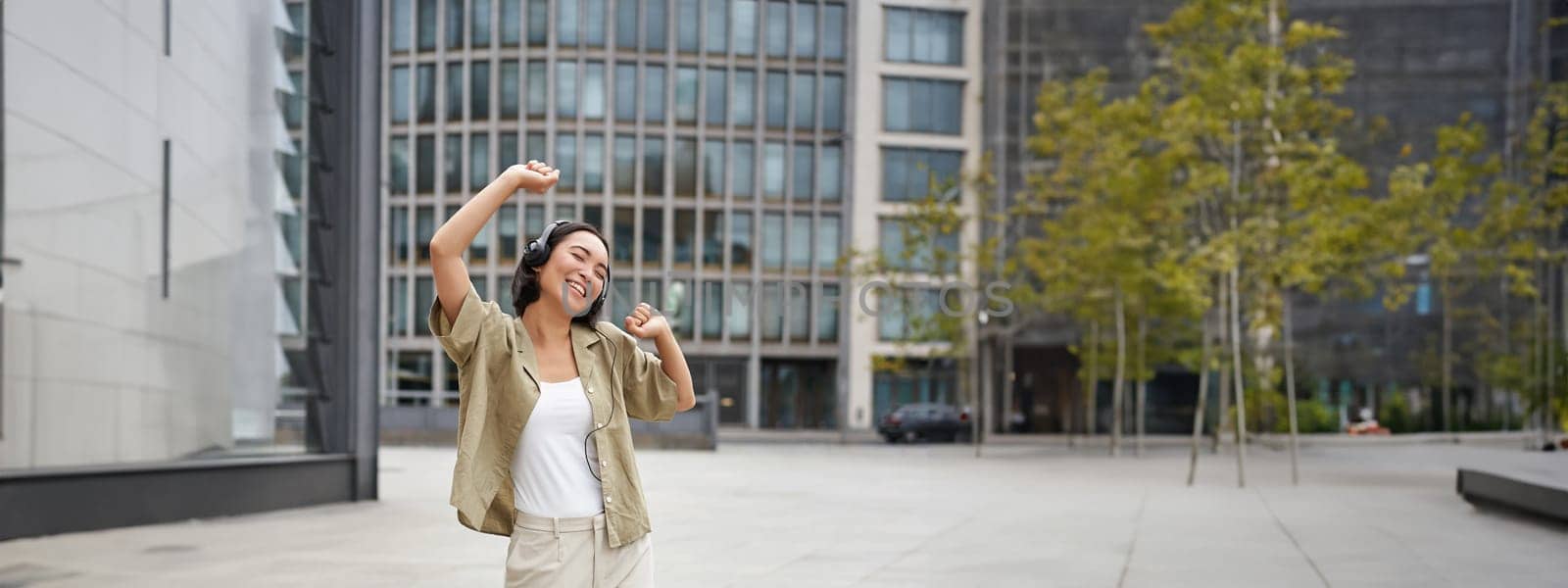 Girl dances on street with headphones on, listens to music and feels happy walking in city.