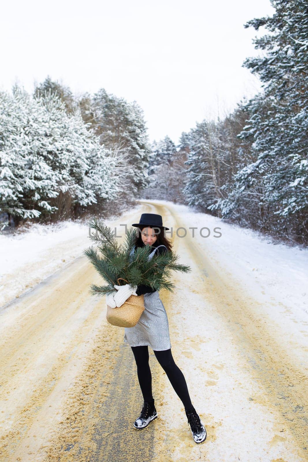 A young girl in a silver dress and hat stands with her back in the middle of a beautiful winter road in the forest