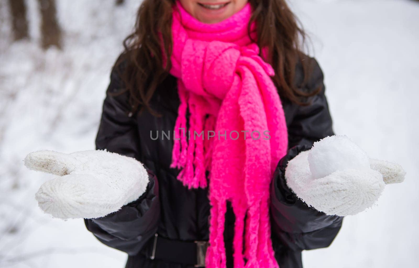 Young woman holding natural soft white snow in her hands to make a snowball, smiling on a cold winter day in the forest, outdoors. by sfinks