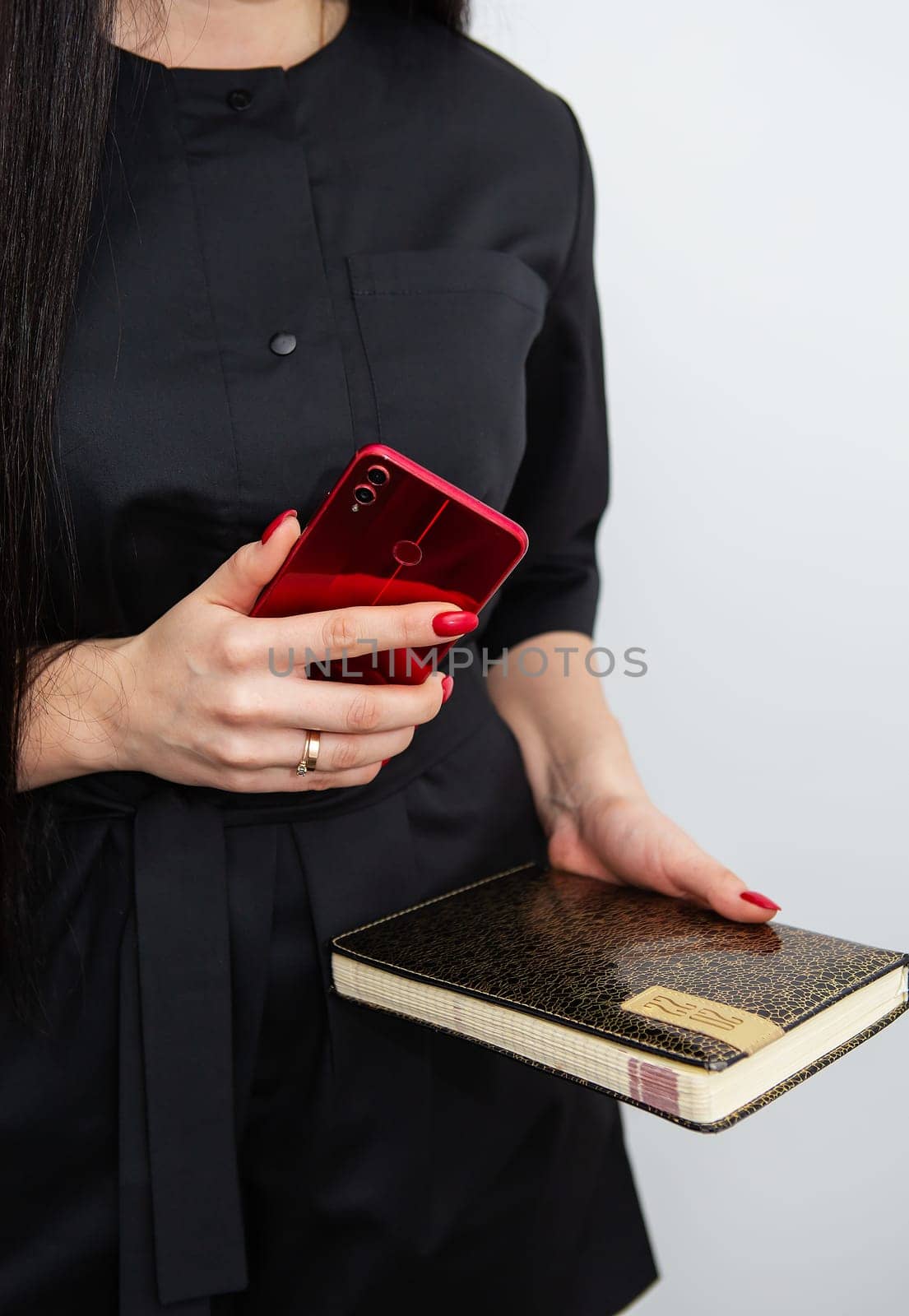 A business woman in a black uniform is standing, holding a smartphone and a notebook about work in her beauty salon. Concept of small business, beauty salon and self care