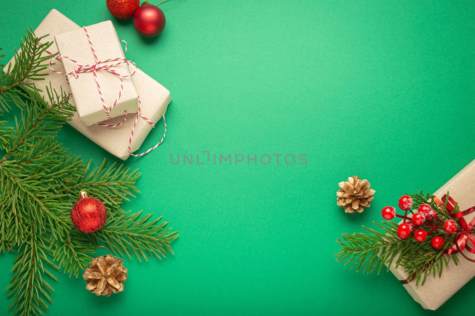 Christmas or New Year celebration green paper festive background with decoration fir tree, present boxes, cones, berries, sparkly red balls. Space for text..