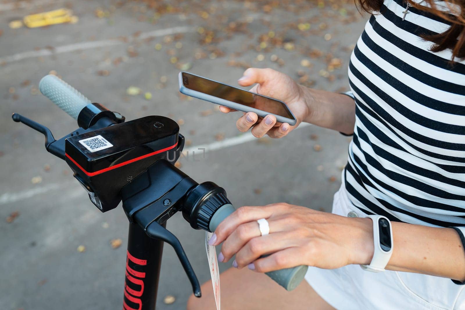 A girl rents an electric scooter with an application on her phone. Self-service electric scooter rental on the street