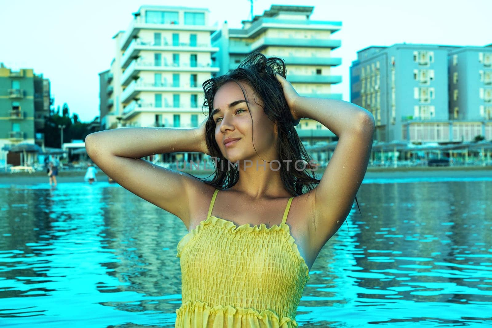 An attractive model with long hair poses with her hands raised behind her head at sunrise.