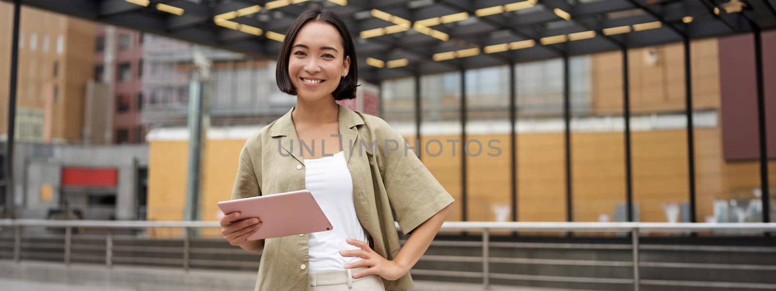 City girl standing with tablet on street, using application, smiling at camera.