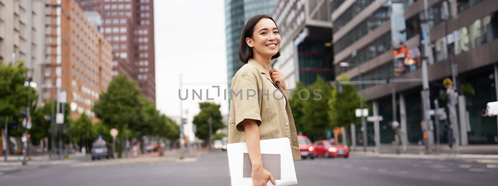 Outdoor shot of asian girl with laptop, going somewhere in city centre, walking on street, going to work.