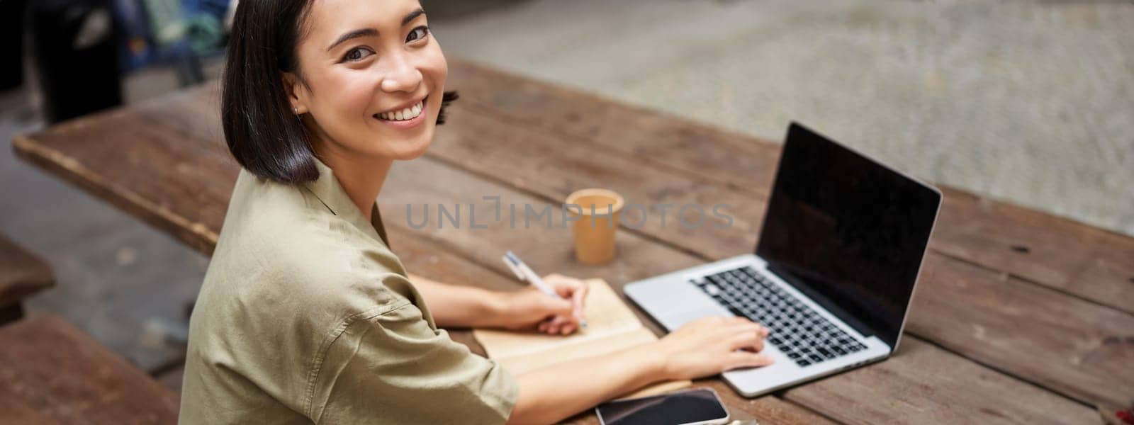 Portrait of young asian woman working on laptop, screen is blank. Girl working outdoors on remote, studying, e-learning and smiling.