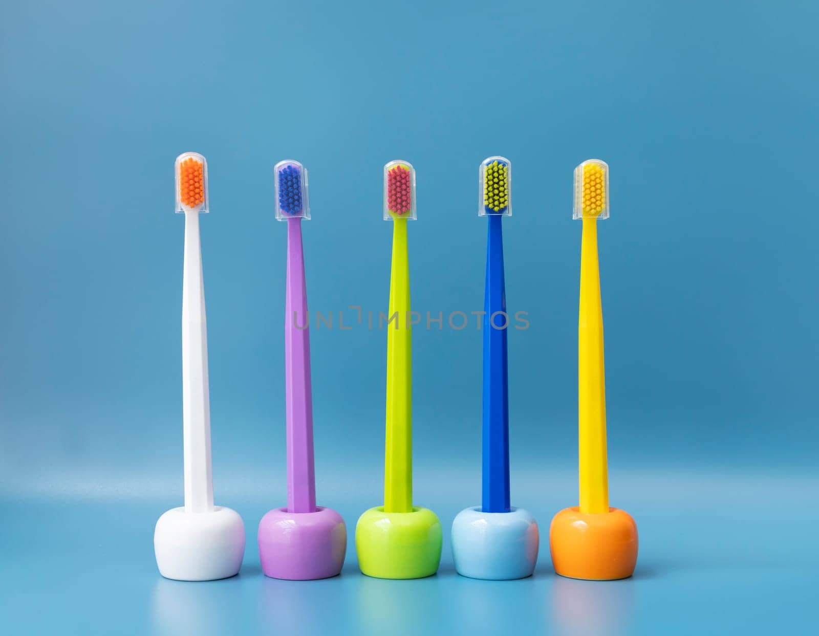 Large Number of Brightly Colored Toothbrushes On Stands, Holder in Row On Blue Background. Morning hygiene, Bathroom accessories. Dental Health Care. Horizontal Plane by netatsi