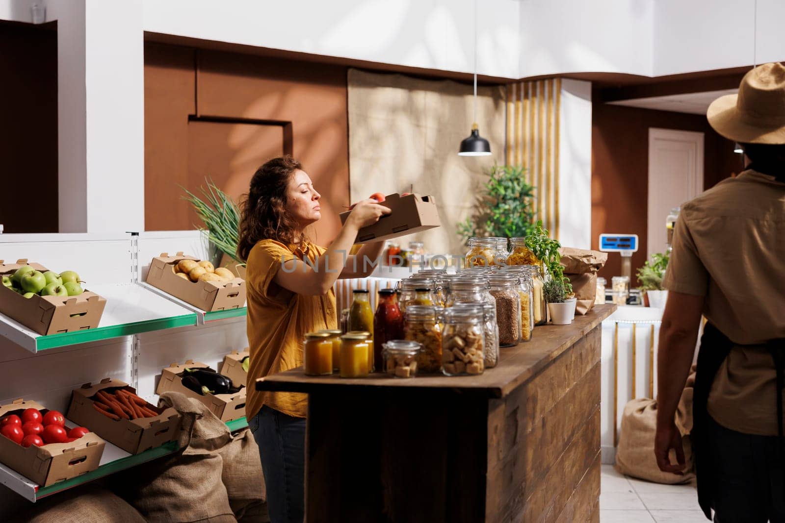 Healthy living woman in zero waste shop looking to buy freshly harvested tomatoes and other vegetables. Customer shopping for ecofriendly groceries in local neighborhood store