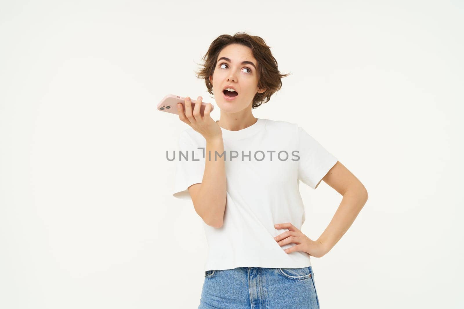 Portrait of woman speaking into speakerphone, taking in microphone, recording voice message, standing over white background.