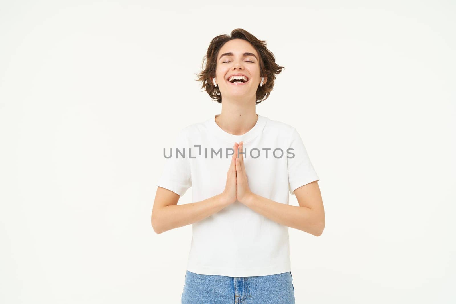 Portrait of mindful young woman, showing namaste, grateful gesture, saying thank you, asking for something and smiling, standing over white background by Benzoix
