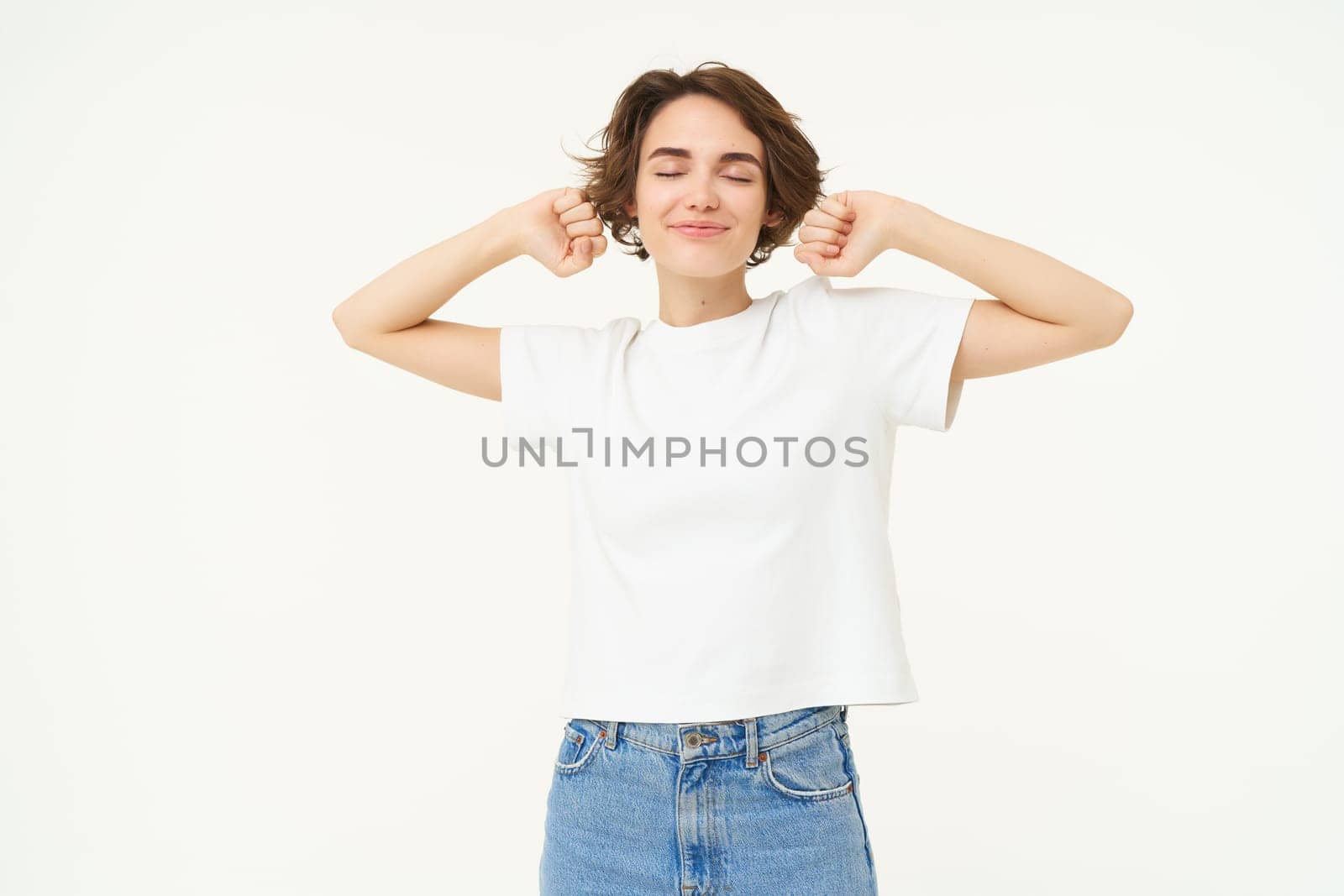 Portrait of pleased brunette woman stretching, feeling good after sleep or taking a nap, waking up, posing over white studio background.