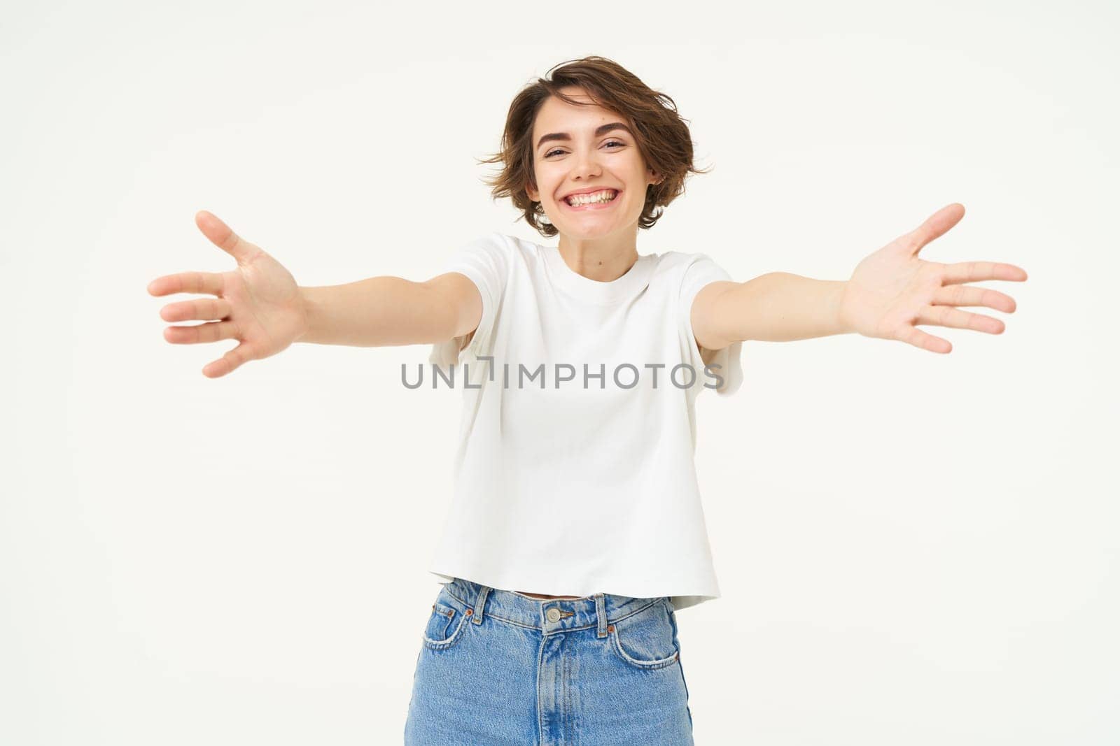 Portrait of beautiful, friendly woman stretching hands, hugging, extending arms for cuddle, embracing someone, standing against white background.