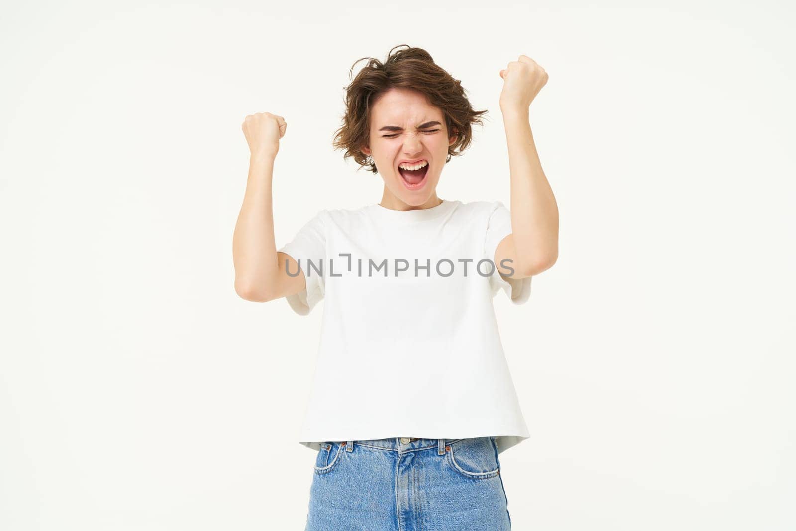 Portrait of woman celebrating, winning prize, triumphing, standing over white studio background.