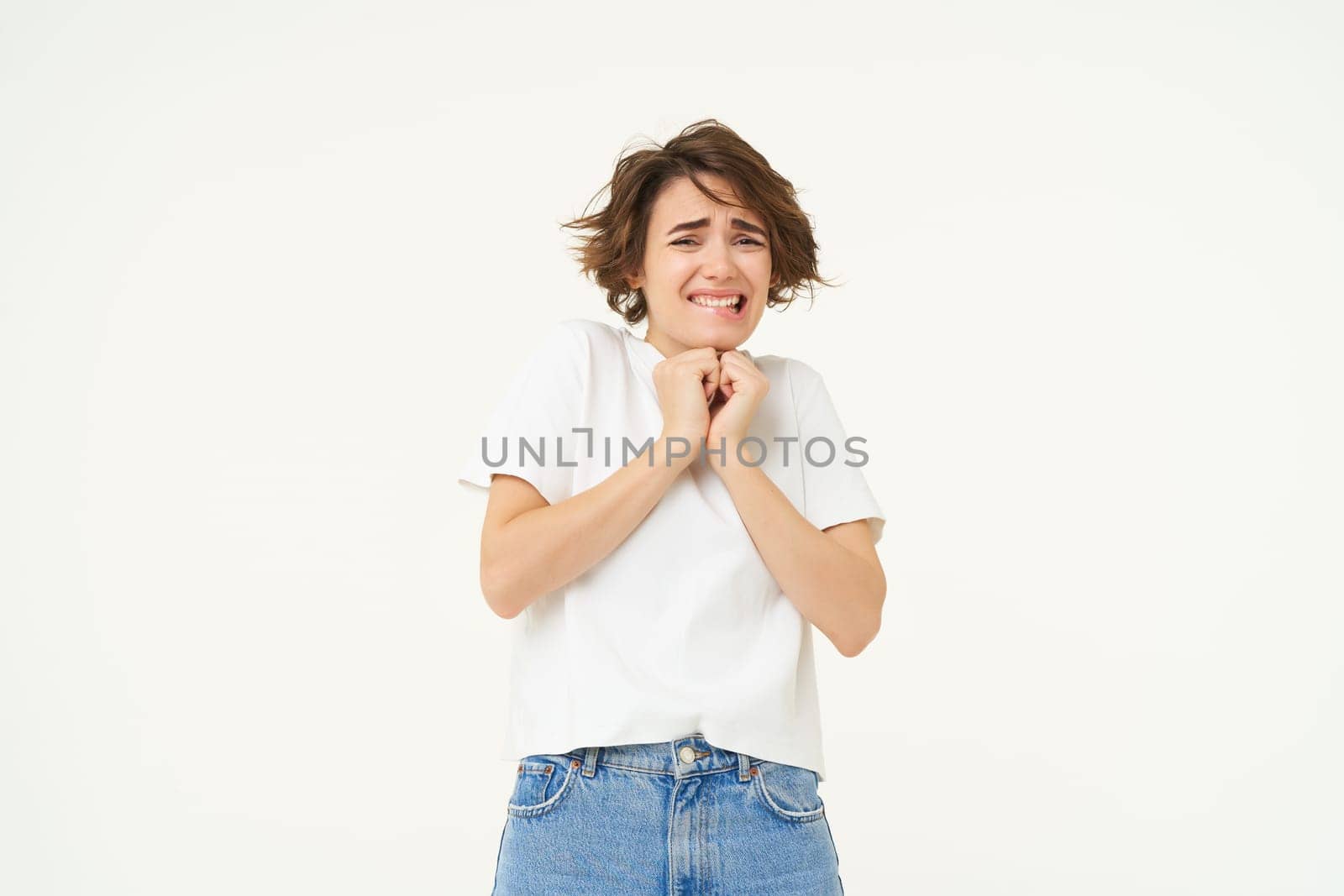 Image of girl jumps from fear, scared, looking frightened, standing against white studio background by Benzoix