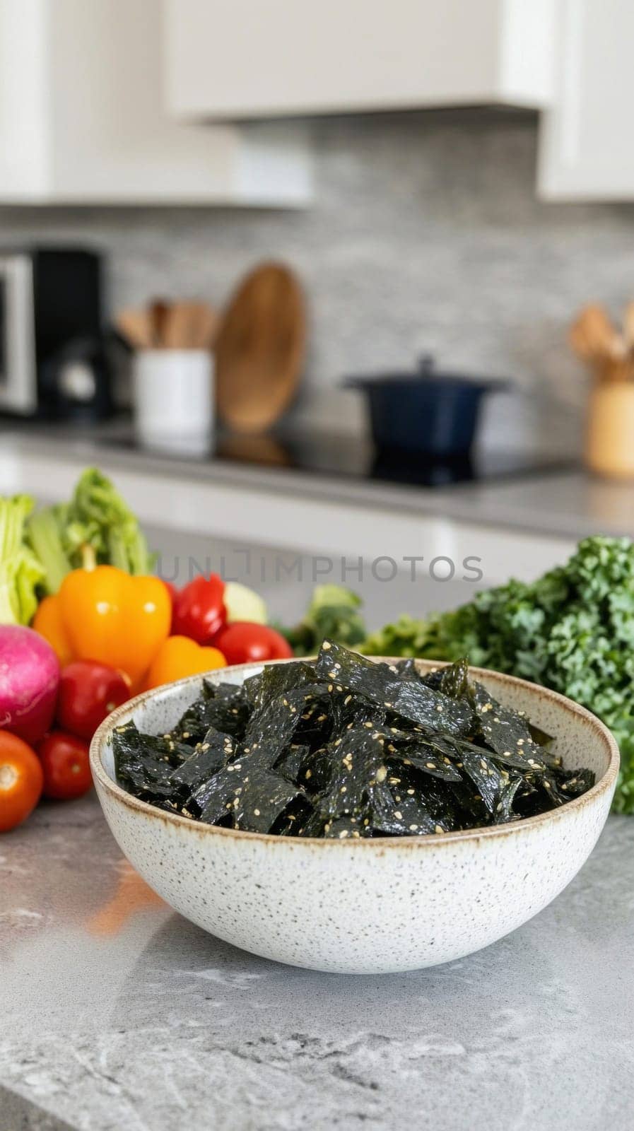 Roasted seaweed sheets seasoned with sesame seeds are served in a bowl on a kitchen counter alongside fresh vegetables, promoting a healthy and delicious snack option