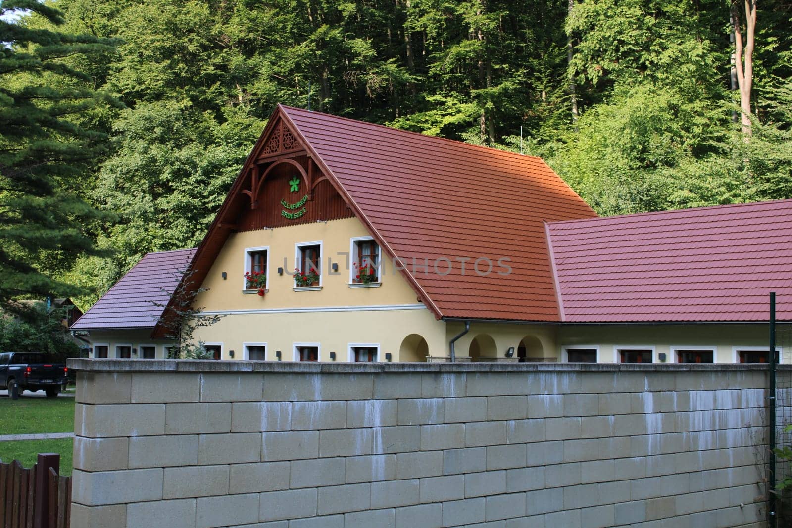 A picturesque house featuring a vibrant red-tiled roof is nestled among dense greenery. The setting offers a peaceful retreat from urban life, showcasing nature's beauty.