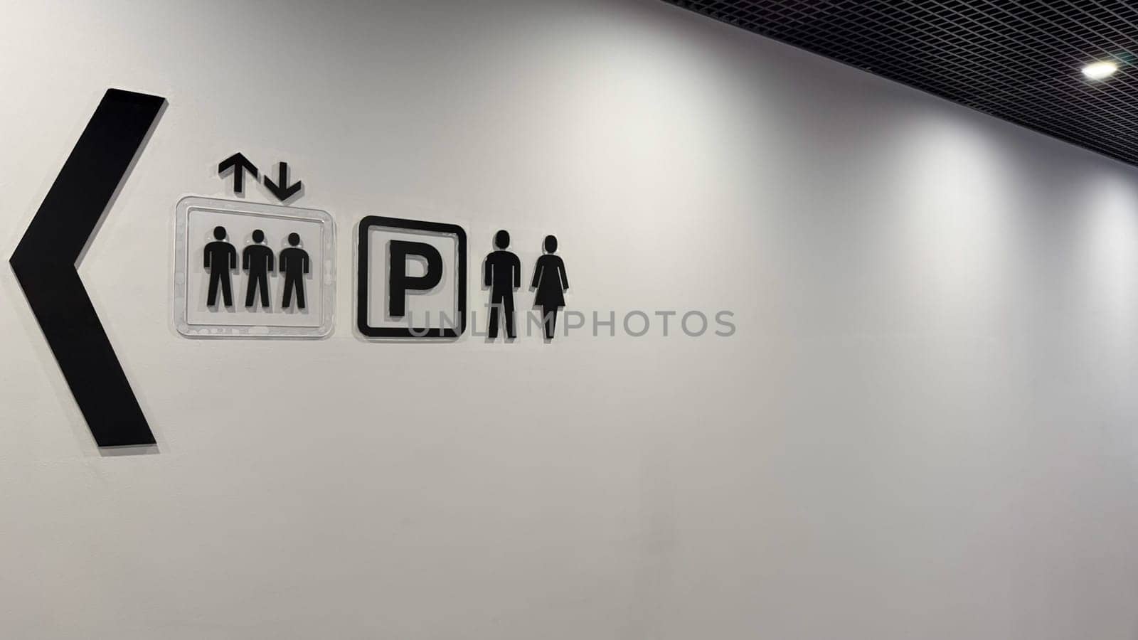 Signs on wall of shopping center with direction of movement to help with orientation, signs in corridor towards elevator, parking and toilet in public building